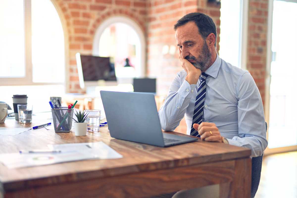 Middle age handsome businessman wearing tie sitting using laptop at the office thinking looking tired and bored with depression problems with crossed arms.